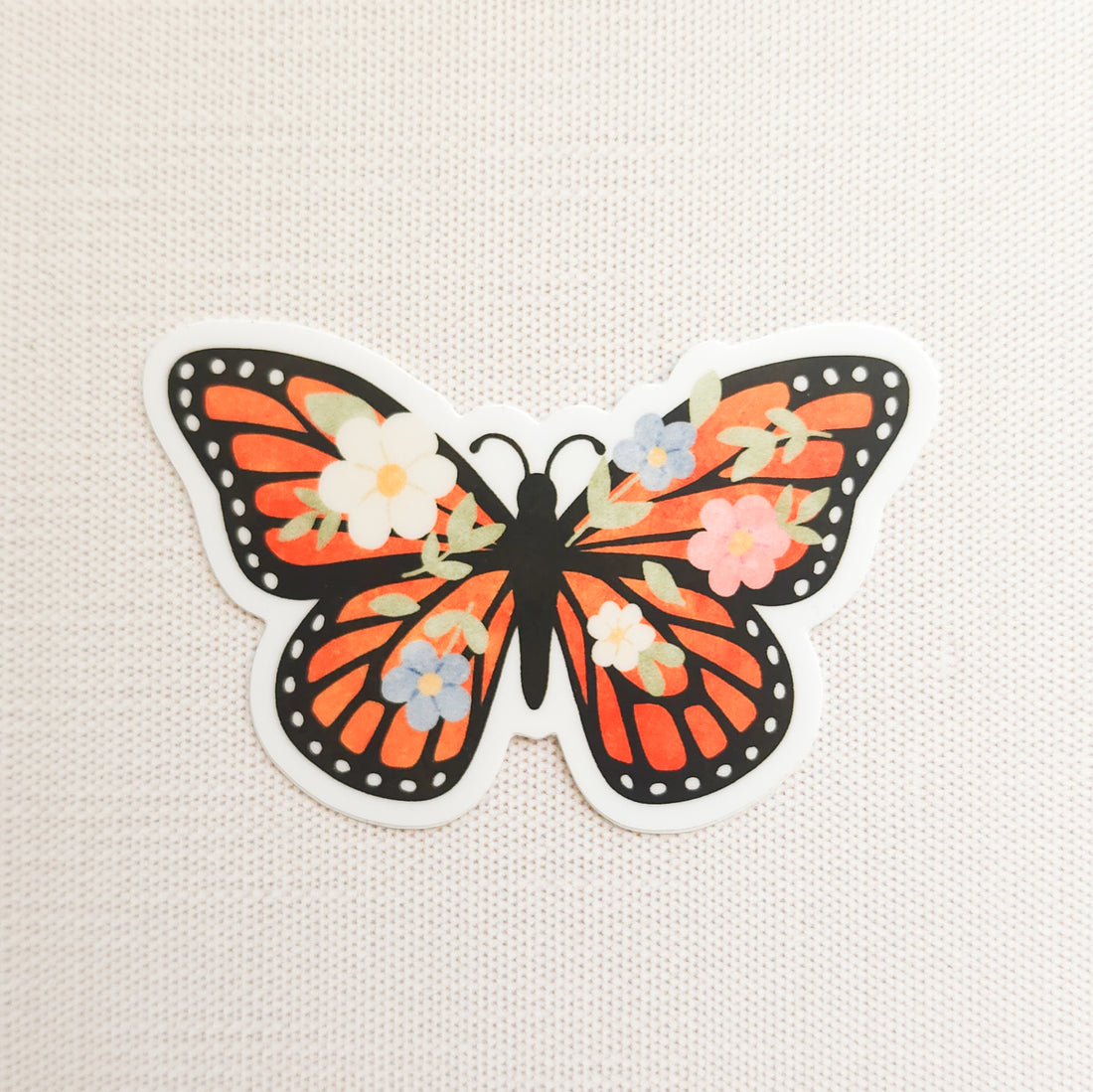 sticker with an illustration of a monarch butterfly with flowers in its wings on a linen background