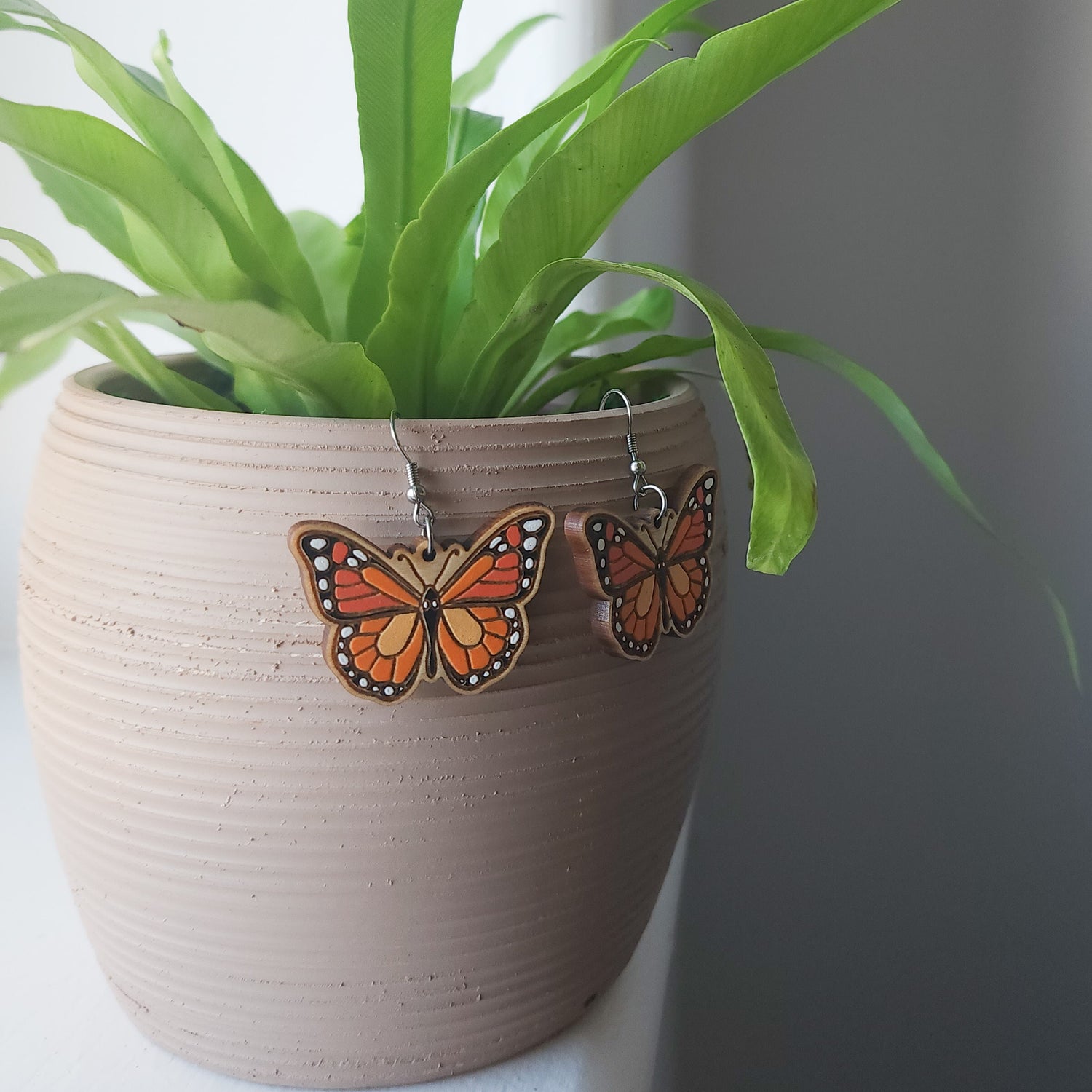 monarch butterfly earrings hanging on a potted plant