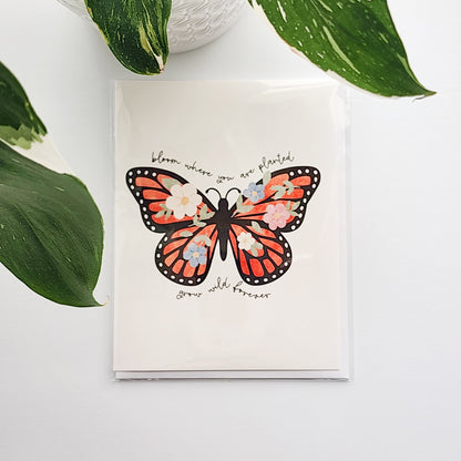 greeting card with an illustrated butterfly and the words bloom where you are planted, grow wild forever. The card is on a white background next to a potted plant