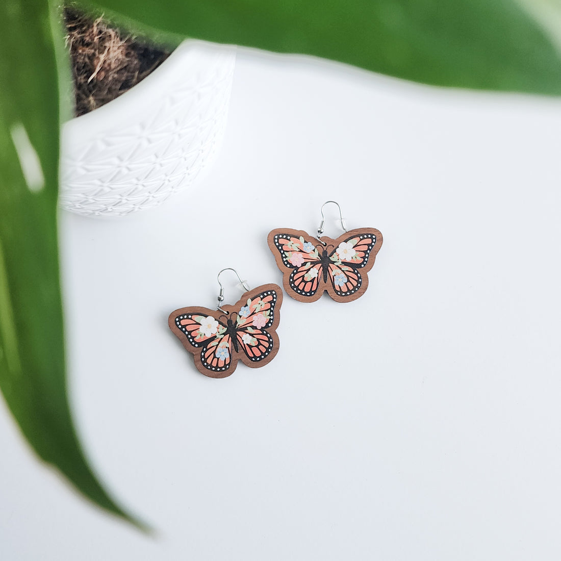 floral butterfly earrings on a white background with a potted plant