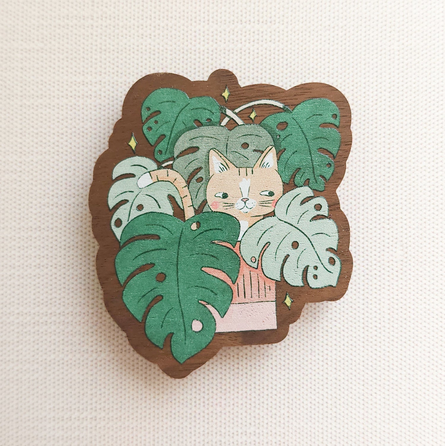 wooden magnet with an image of a cat in a monstera plant on a linen background