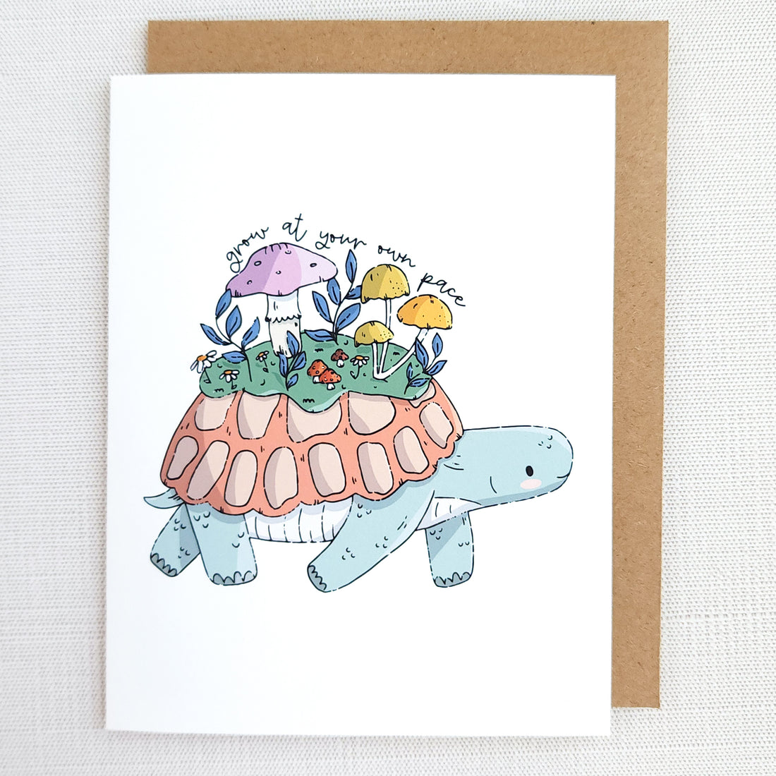 Greeting card with a turtle illustration carrying plants and mushrooms on its shell and the words grow at your own pace