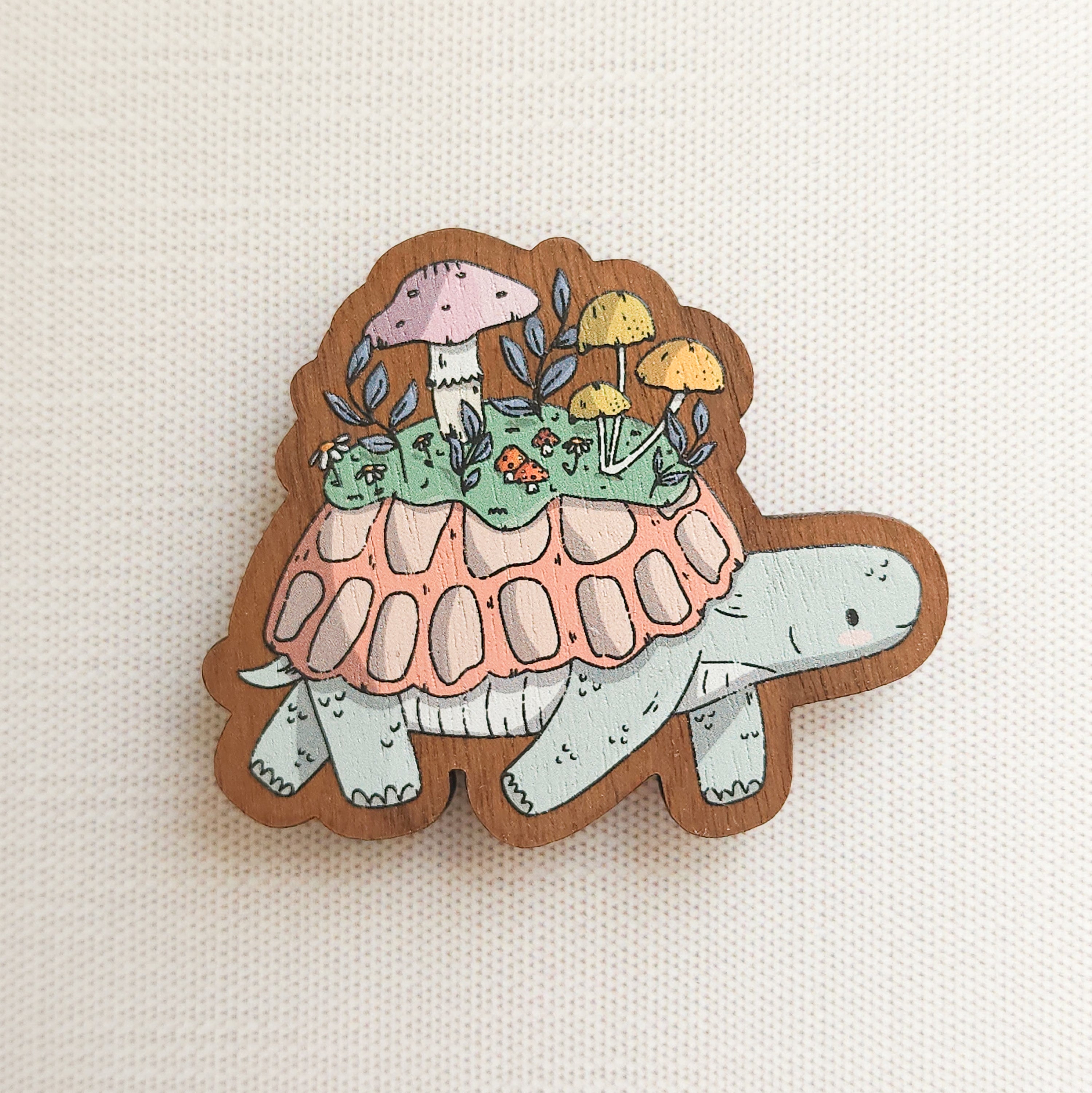 wooden magnet with an illustration of a turtle with a mushroom meadow on its back on a linen background