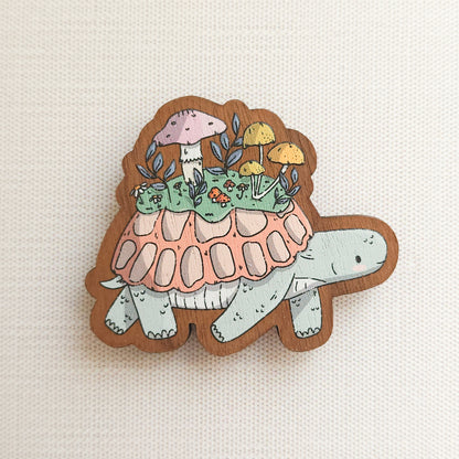 wooden magnet with an illustration of a turtle with a mushroom meadow on its back on a linen background