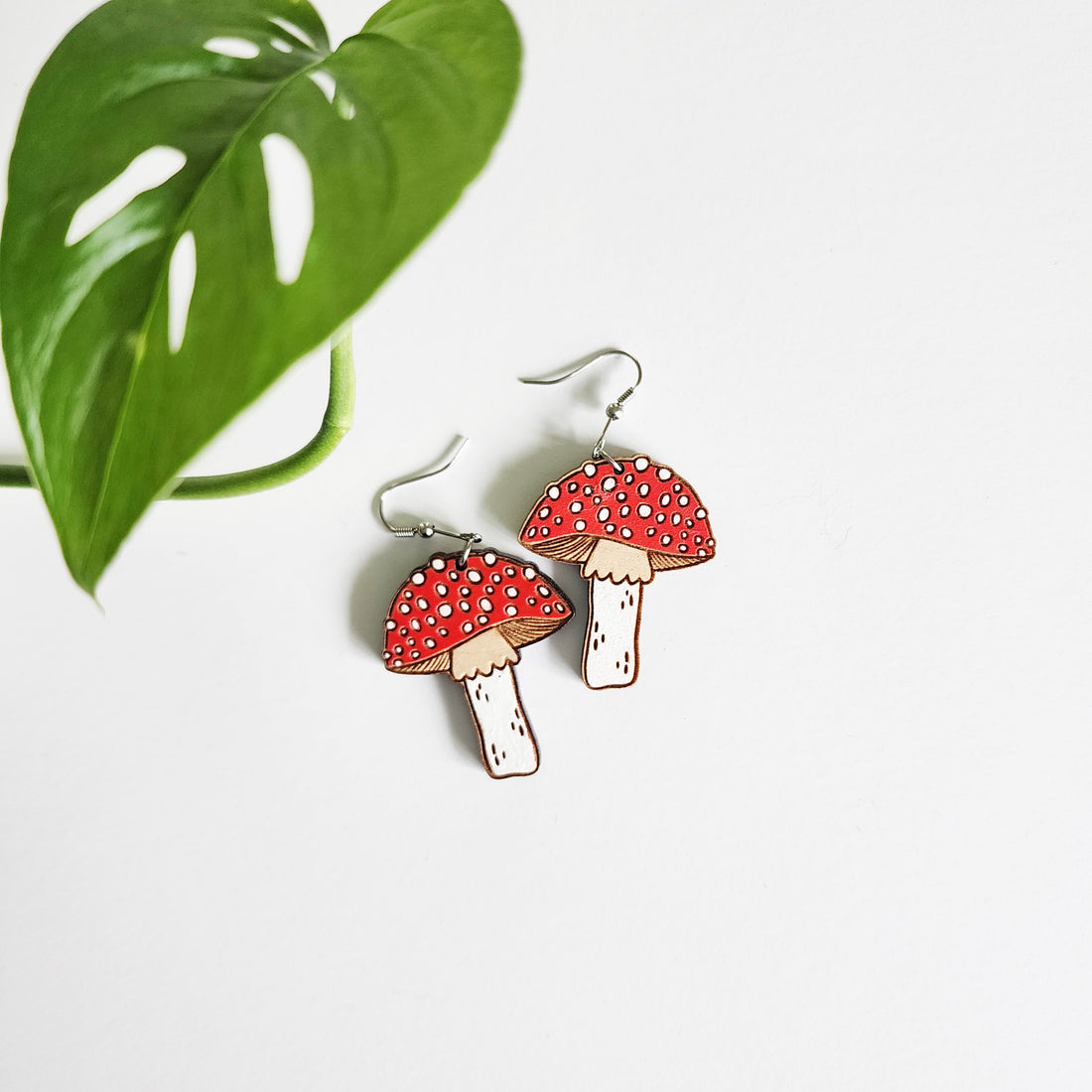 pair of mushroom earrings on a white background next to a leaf