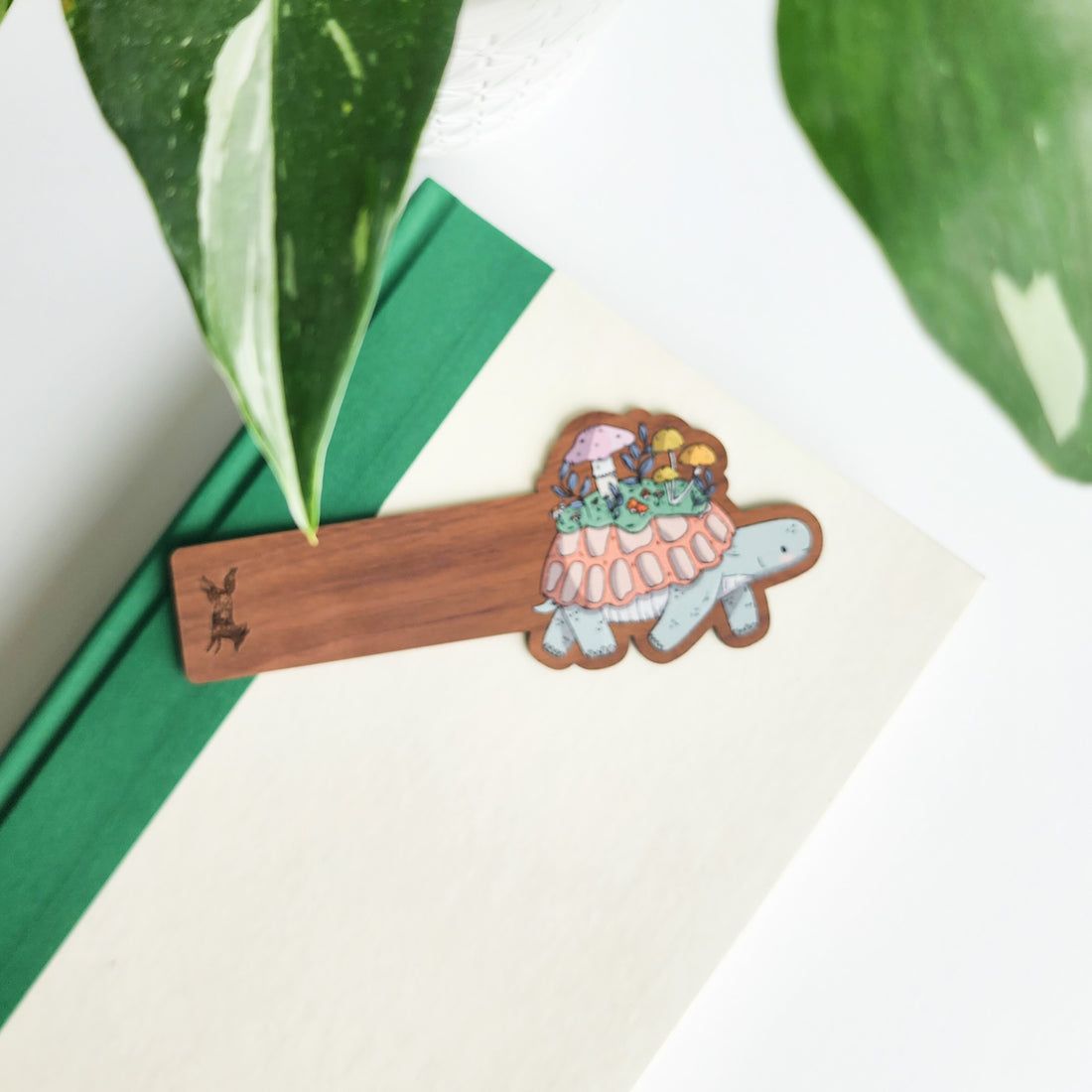 Wooden bookmark with a turtle design on a white surface with green leaves in the background