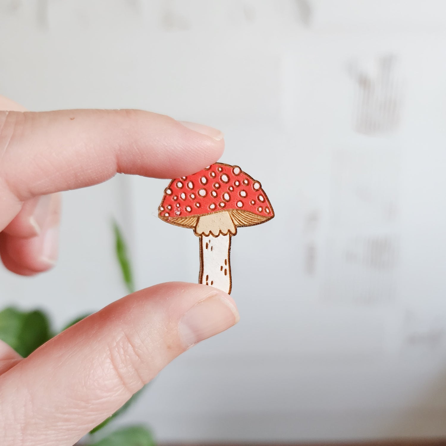 red and white mushroom pin held between two fingers