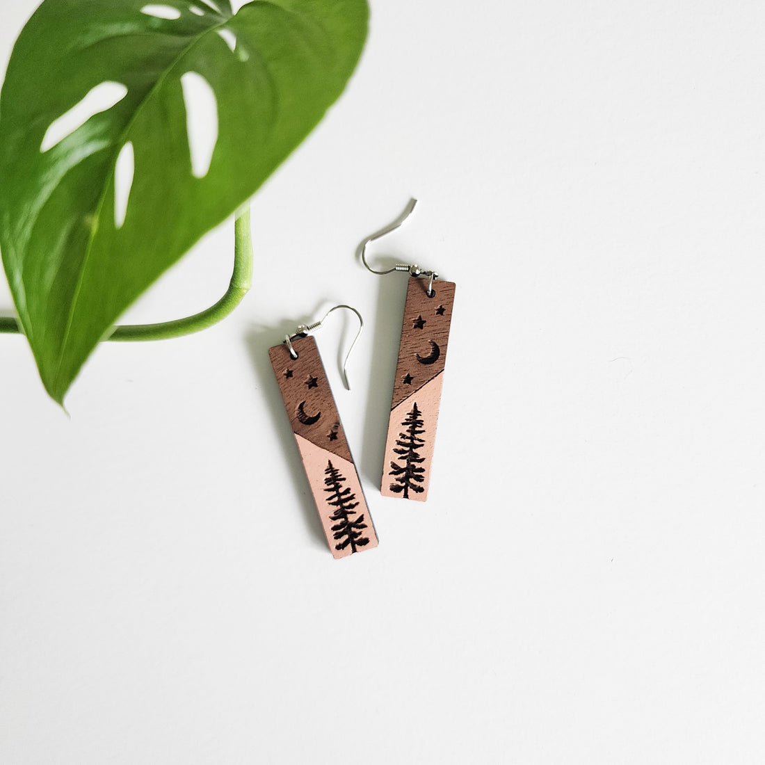 pair of starry woods earrings on a white background next to a leaf