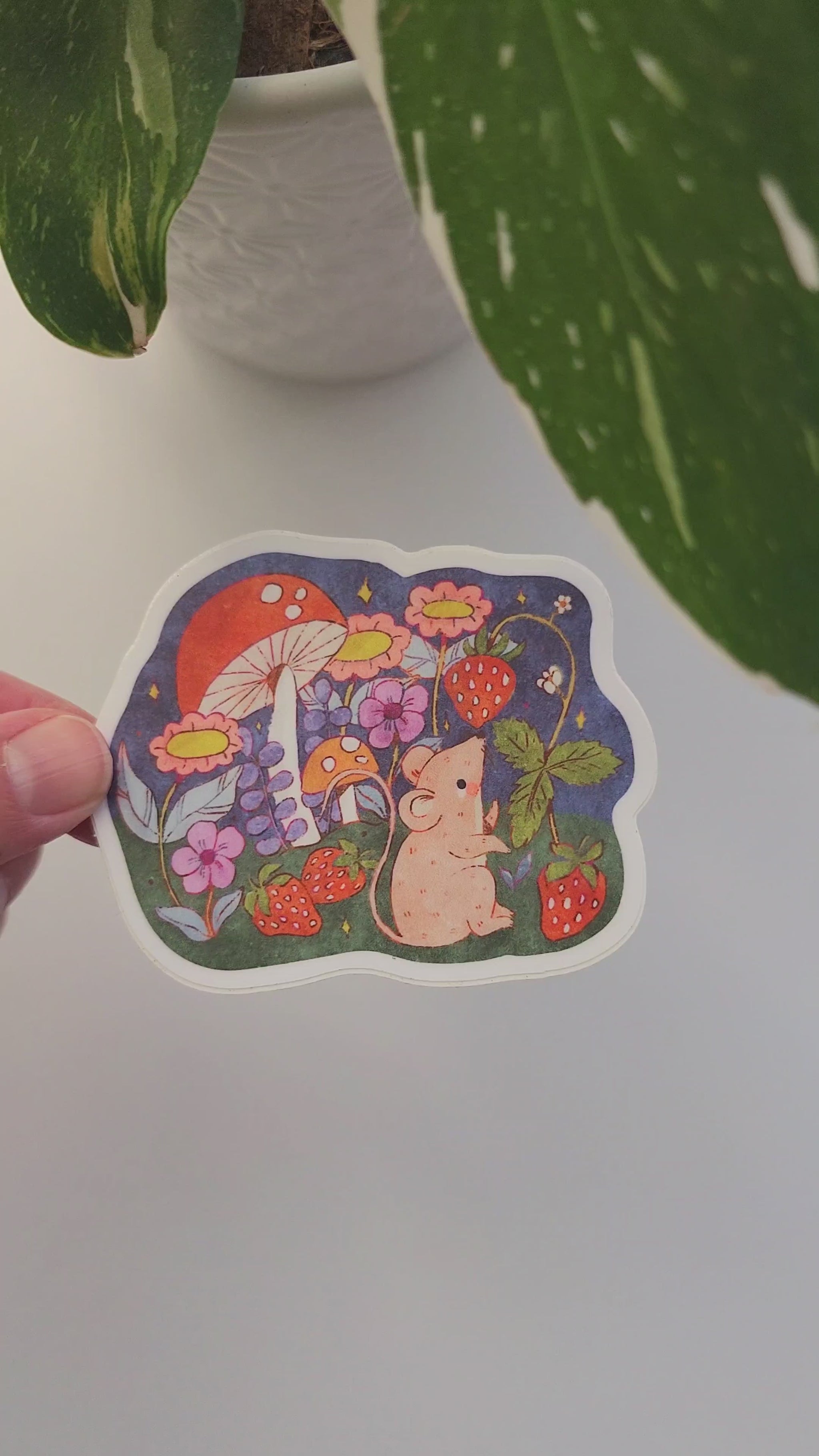 video of strawberry mouse sticker next to a plant