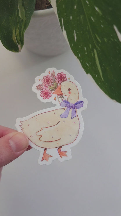 video of a goose blooms sticker held in a hand next to a potted plant