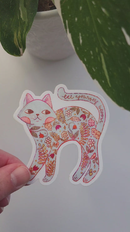 video of a cat sticker held in a hand next to a potted plant