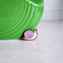 wooden snail pin with purple shell and pink body sitting in fron of a green case