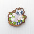 Wooden magnet featuring a curious raccoon surrounded by white moonflowers, green leaves, and tiny golden stars, printed on walnut wood and photographed on a neutral fabric background.