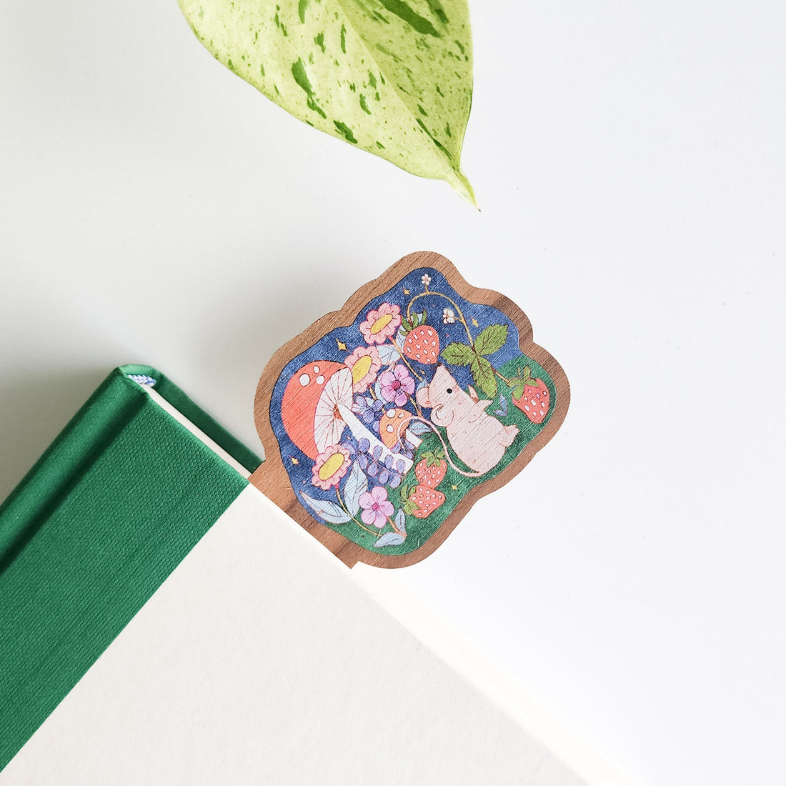 Decorative bookmark with a strawberry mouse and mushrooms on a green book