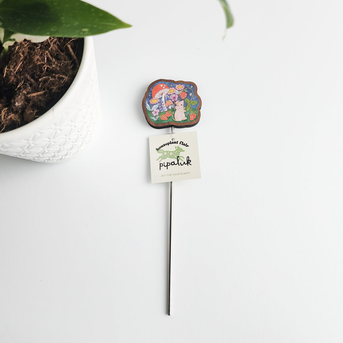 mouse plant pick with a pipaluk tag next to a potted plant on a white background