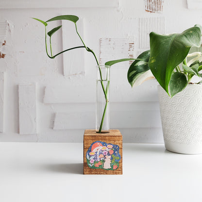 wooden propagation station with a mouse picking strawberries. There is a green plant cutting in a glass tube on a white background