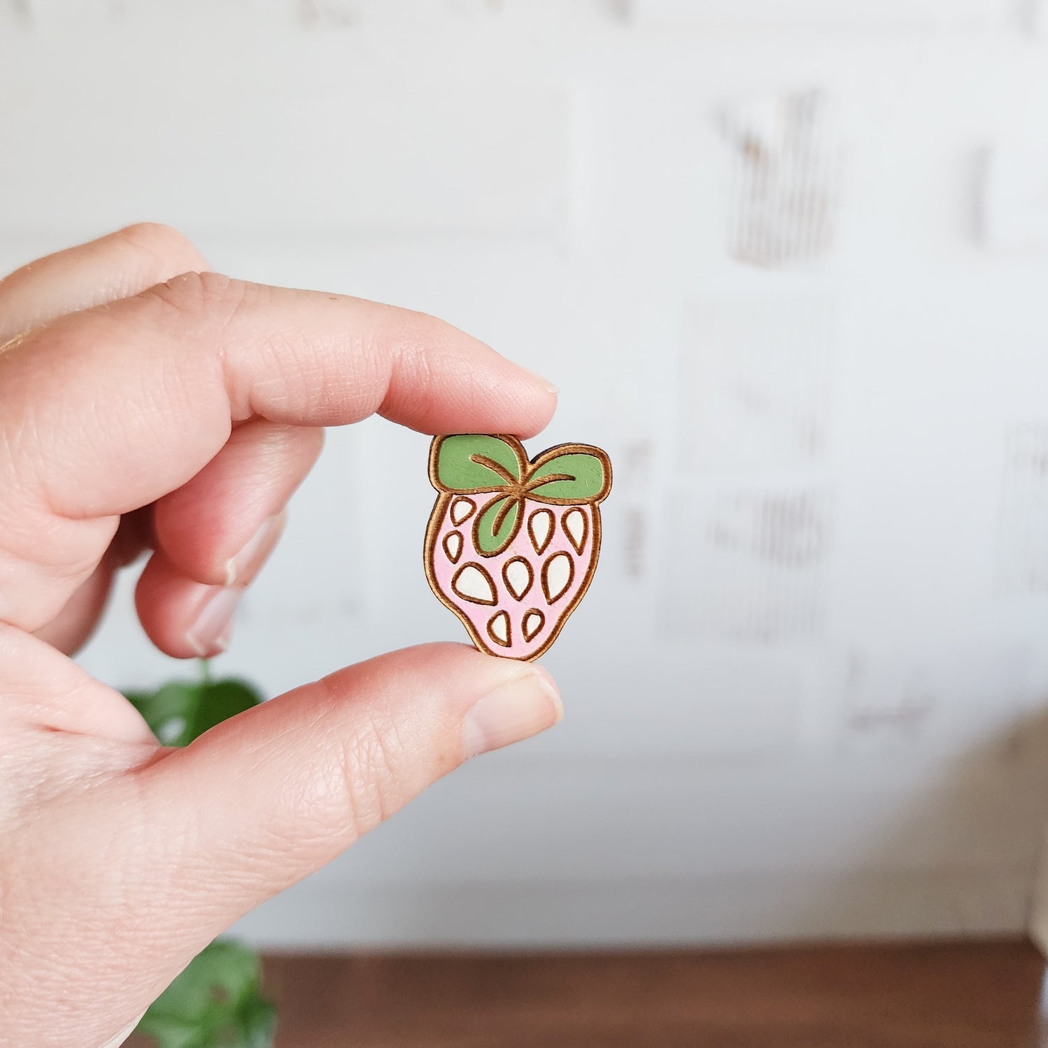 pink and green strawberry pin held between two fingers
