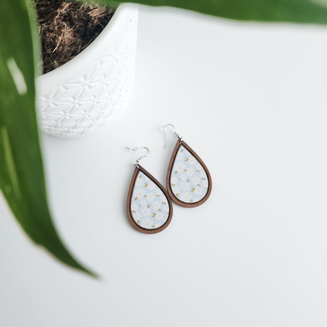 blue floral earrings on a white background next to a potted plant